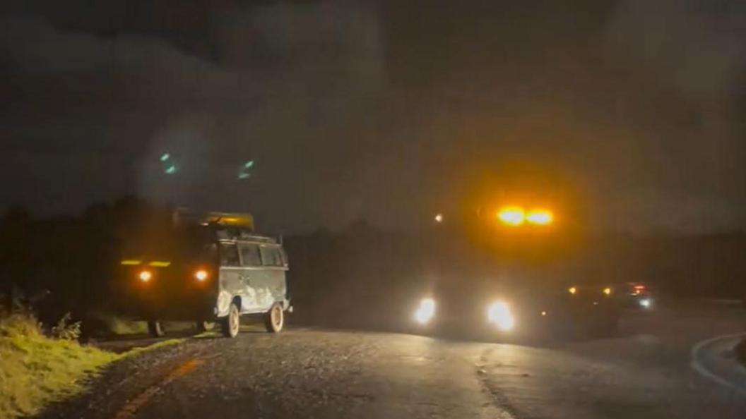 A VW campervan by the side of the road at night with a pick-up truck.